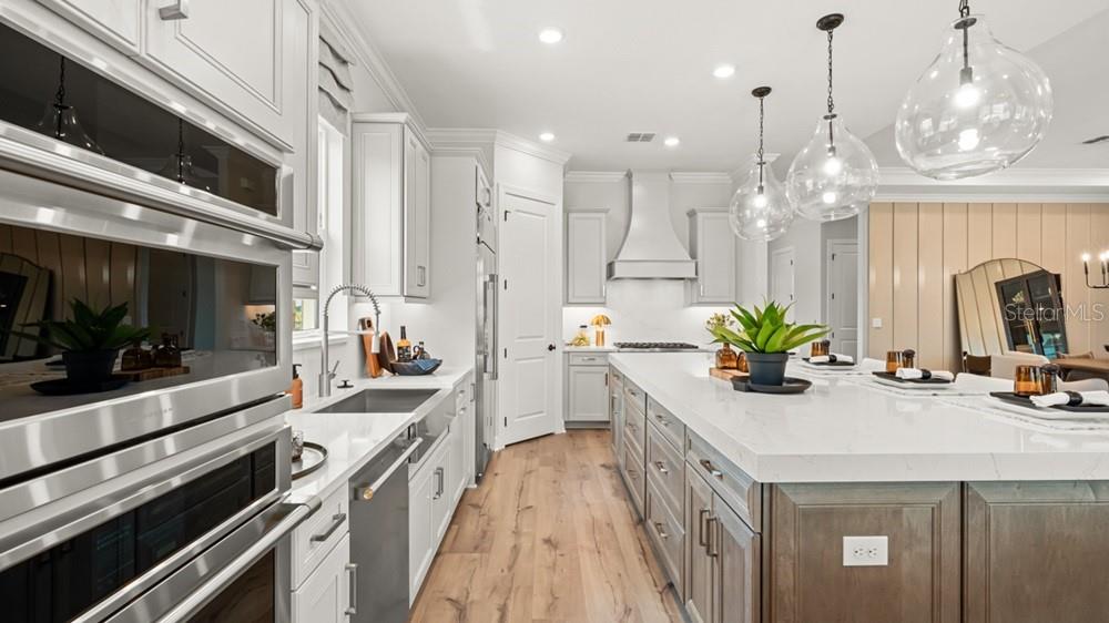 A modern kitchen features white cabinetry, a large quartz island, stainless appliances, and pendant lighting — 26112 ASPARANO AVENUE, ENGLEWOOD, FL