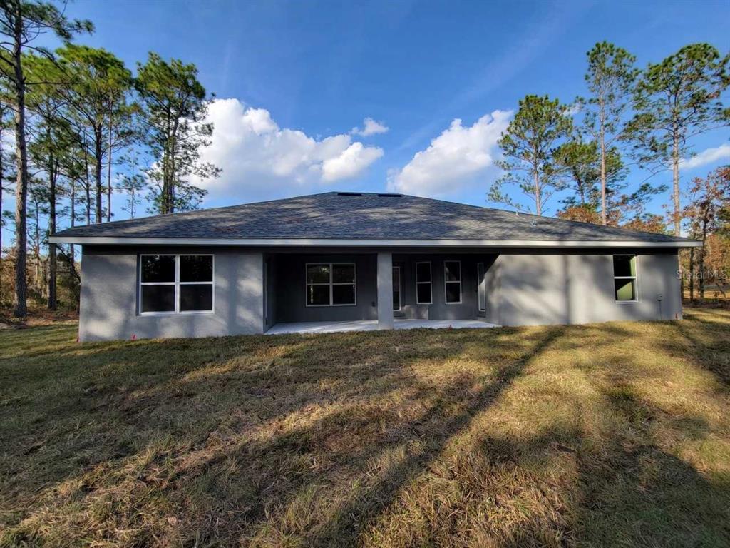 The rear exterior of a single-story gray stucco house features a covered patio and yard — 4404 SW 110TH STREET, OCALA, FL