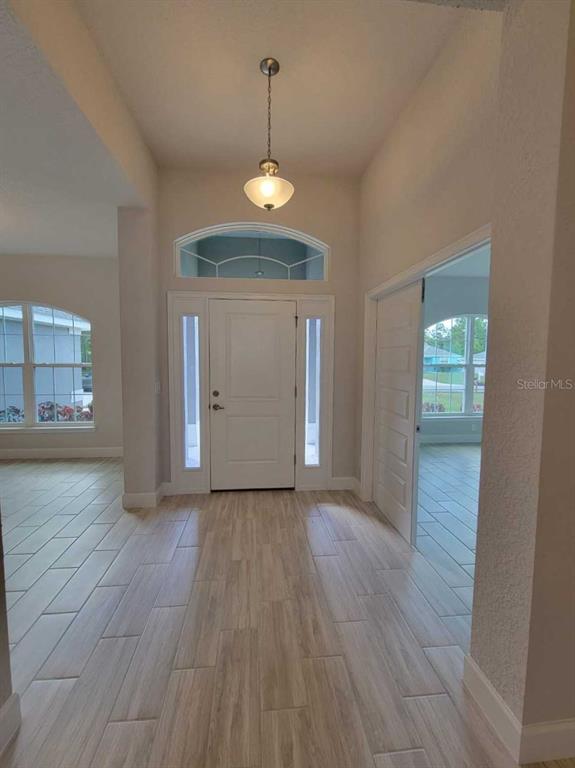 An entryway with light wood-look tile flooring, a white front door, and a hanging pendant light — 4404 SW 110TH STREET, OCALA, FL