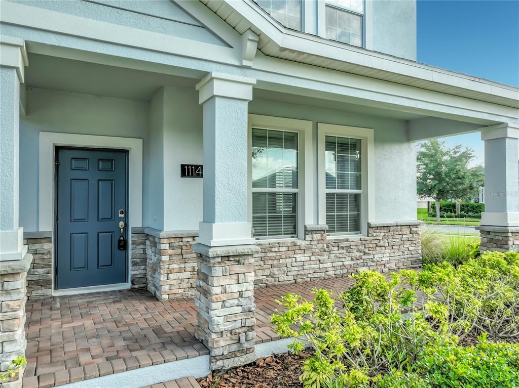 A covered front porch features a blue door, stone accents, and brick pavers — 11143 SYCAMORE WOODS DRIVE, ORLANDO, FL