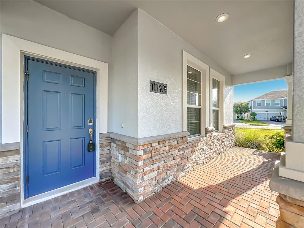 A blue front door opens onto a brick porch with stone veneer siding and windows — 11143 SYCAMORE WOODS DRIVE, ORLANDO, FL