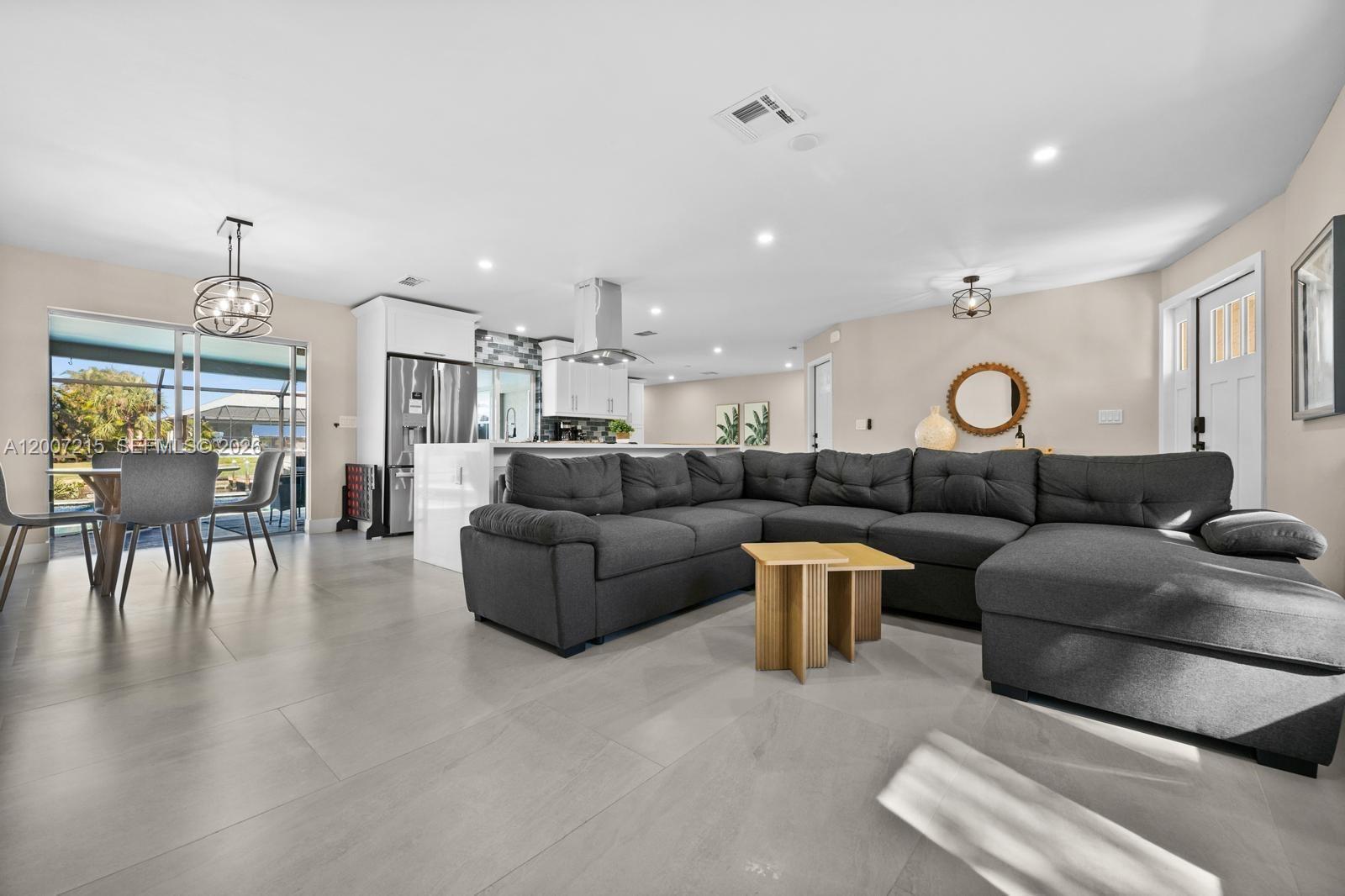 A modern open-concept living room and kitchen feature gray tile floors and a large sectional — 117 SE 40 TER, Cape Coral FL 33904, CAPE CORAL, FL