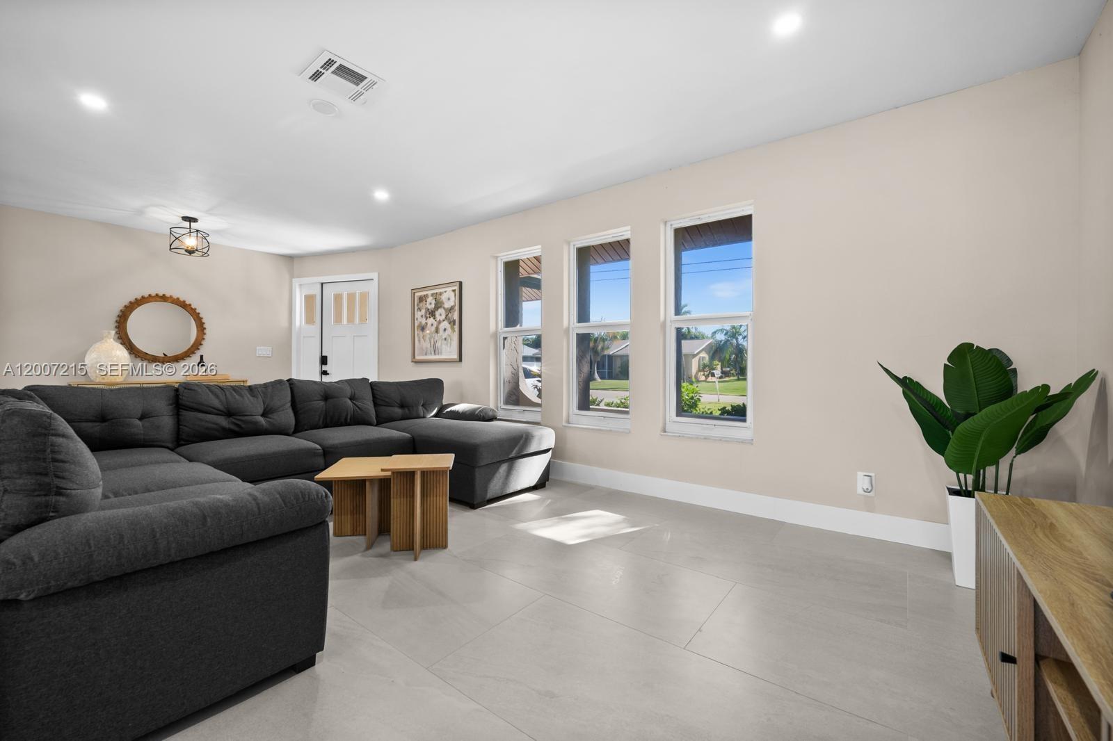 A living room features a gray sectional sofa, light tile flooring, and three large windows — 117 SE 40 TER, Cape Coral FL 33904, CAPE CORAL, FL
