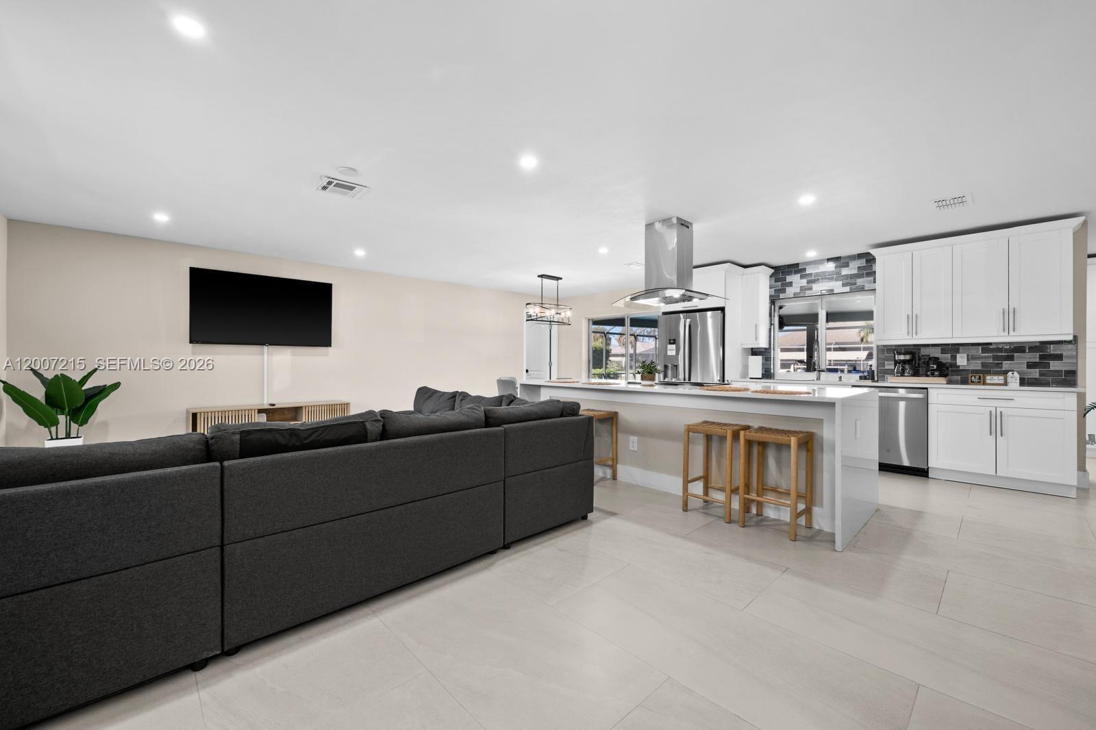 A modern open-concept kitchen and living area featuring white cabinetry and a gray sectional sofa — 117 SE 40 TER, Cape Coral FL 33904, CAPE CORAL, FL