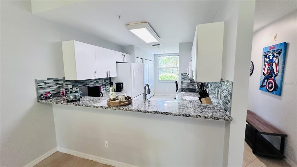 A kitchen features white cabinets, granite countertops, a tiled backsplash, and a breakfast bar — 4640 TOWER HILL LANE UNIT 2315, SARASOTA, FL