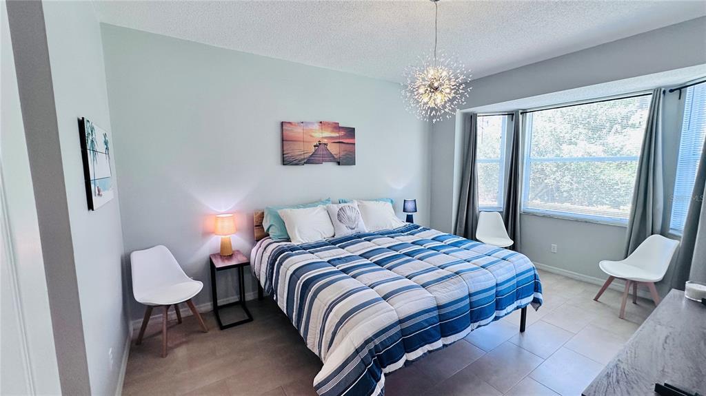 A bedroom features a striped blue and white comforter, a modern chandelier, and two chairs — 4640 TOWER HILL LANE UNIT 2315, SARASOTA, FL
