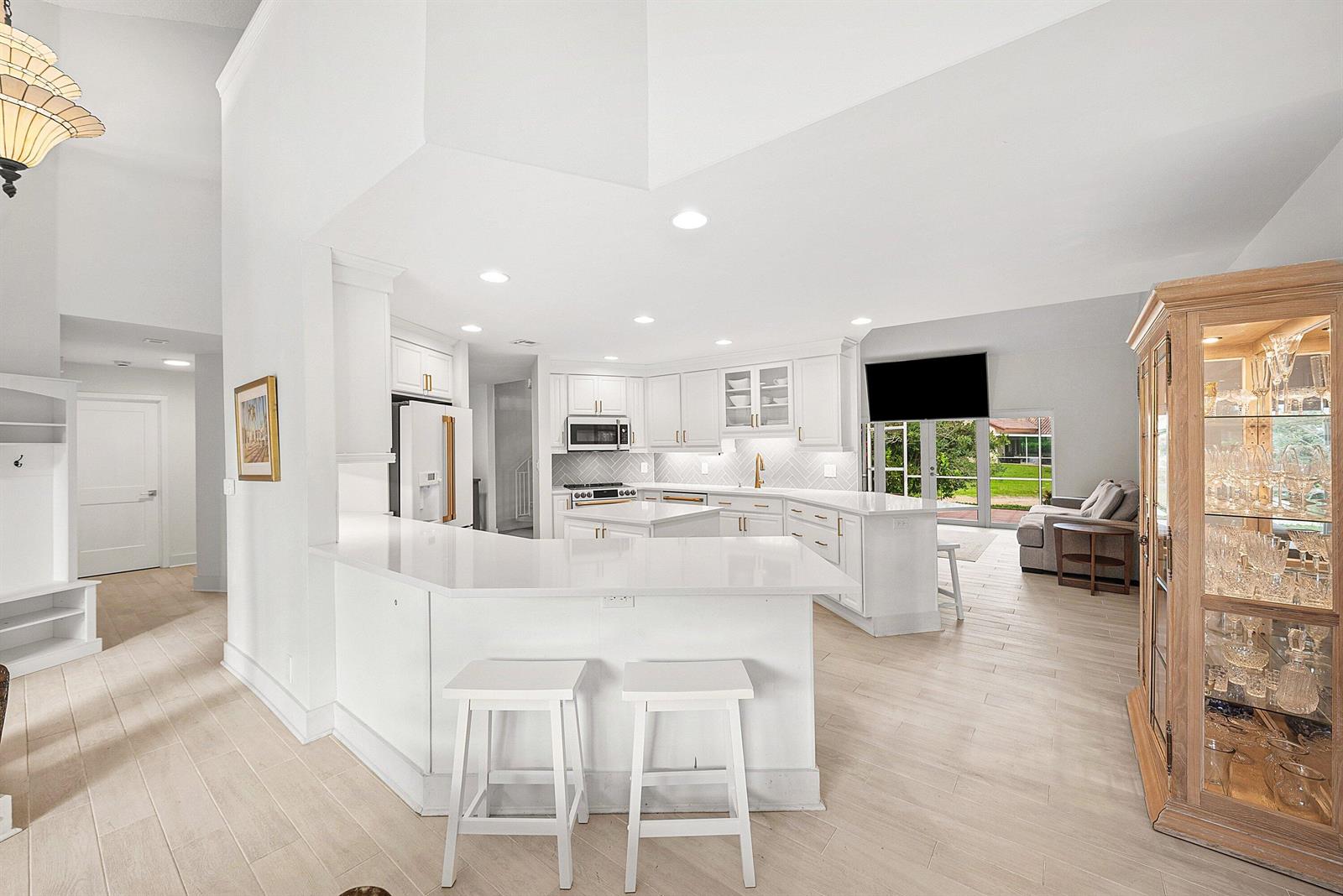 A bright kitchen features white cabinetry, a central island, and a light-colored herringbone backsplash — 23373 Water Circle, Boca Raton FL 33486, BOCA RATON, FL