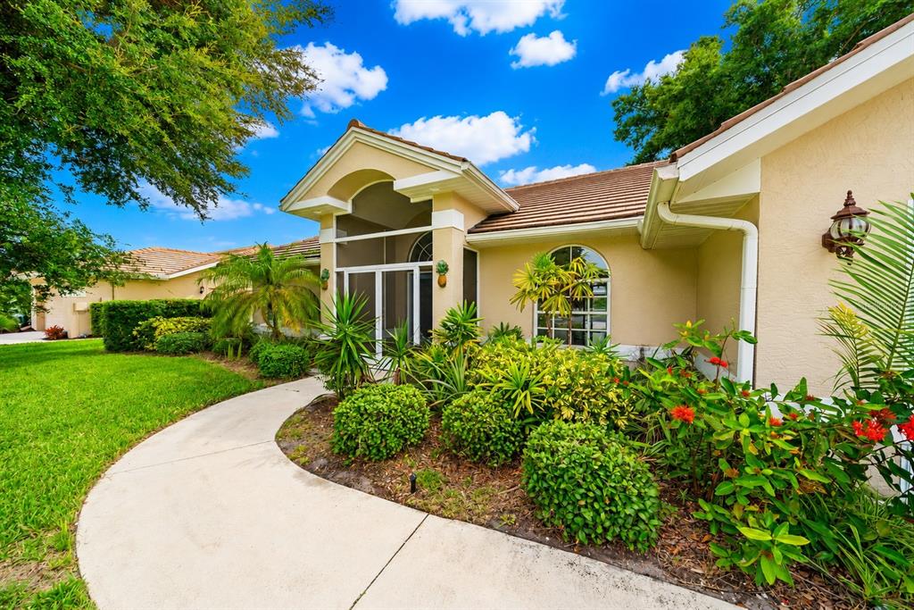 A beige house exterior features a curved walkway, a screened entryway, and landscaped garden beds — 555 PARK ESTATES SQUARE, VENICE, FL
