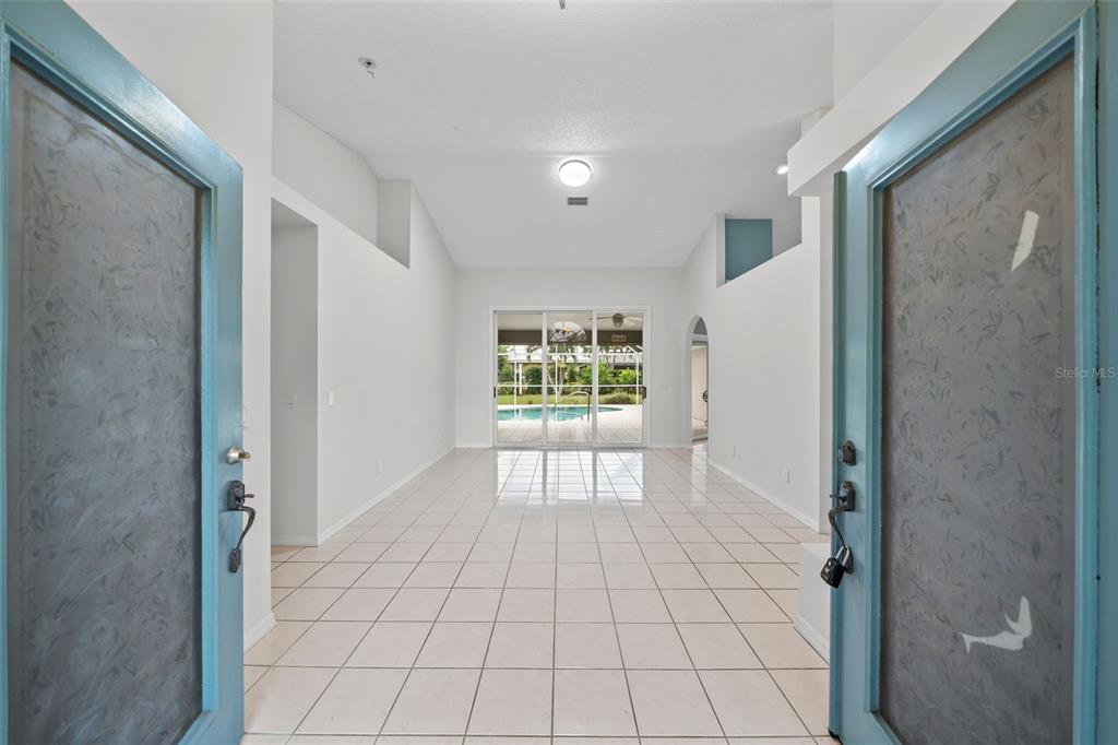 An entryway opens into a bright, tiled living area with vaulted ceilings and sliding glass doors — 555 PARK ESTATES SQUARE, VENICE, FL