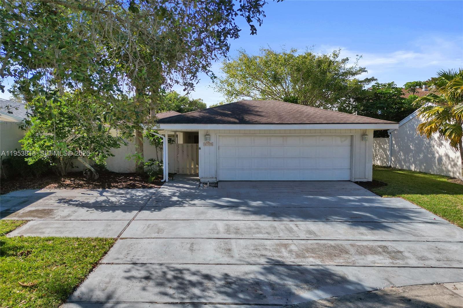 A single-story house features a white garage door, a concrete driveway, and surrounding trees — 17115 Bay St, Jupiter FL 33477, JUPITER, FL
