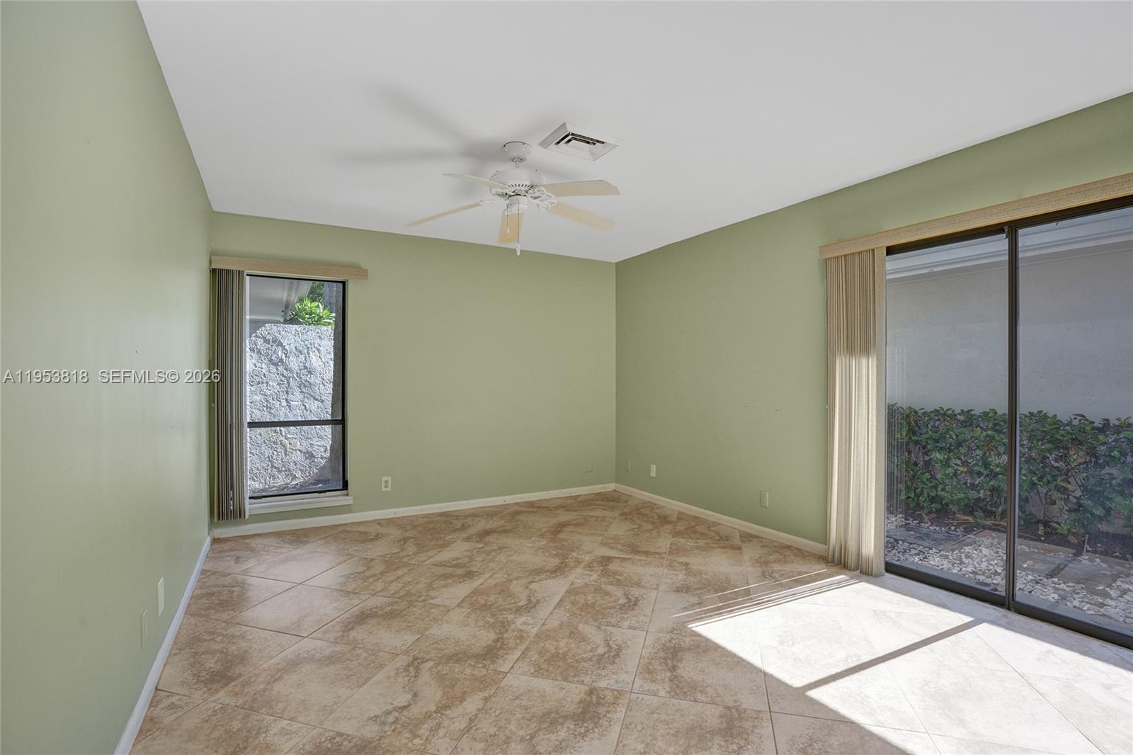 An empty room features sage green walls, tile flooring, a ceiling fan, and sliding glass doors — 17115 Bay St, Jupiter FL 33477, JUPITER, FL