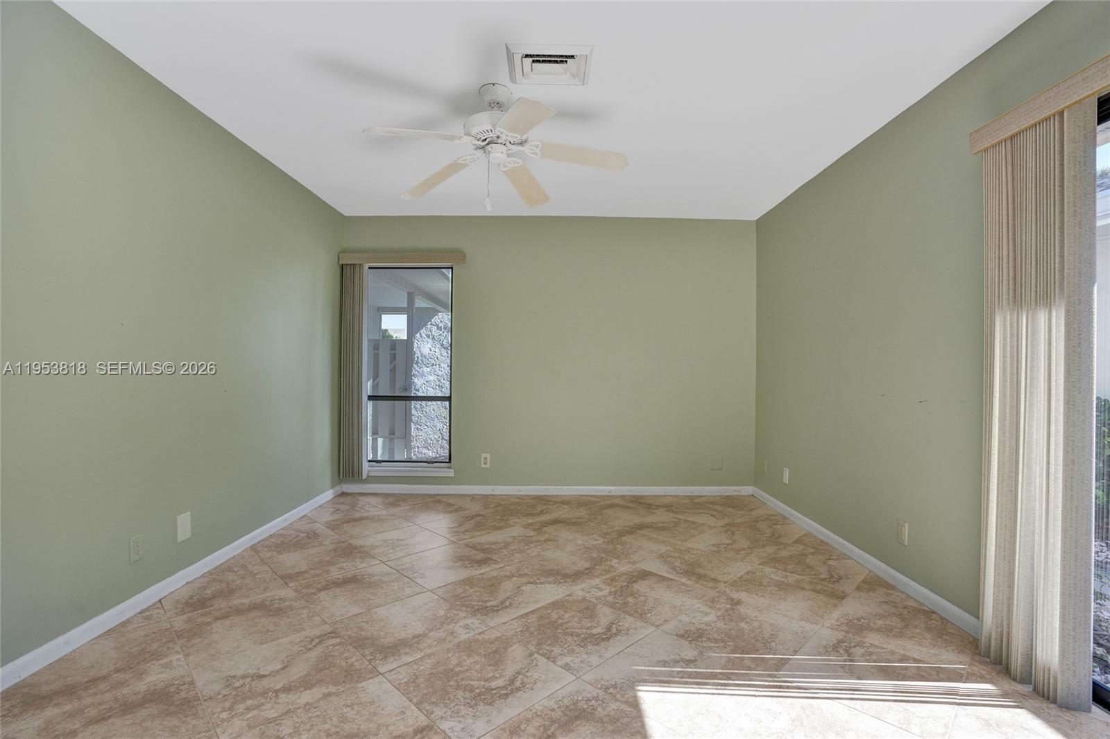 An empty room features light green walls, tan tile flooring, a ceiling fan, and vertical blinds — 17115 Bay St, Jupiter FL 33477, JUPITER, FL