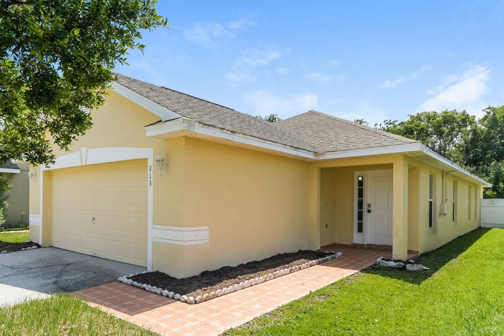 A yellow single-story house with a two-car garage and a tiled walkway — 213 OWENSHIRE CIRCLE, KISSIMMEE, FL