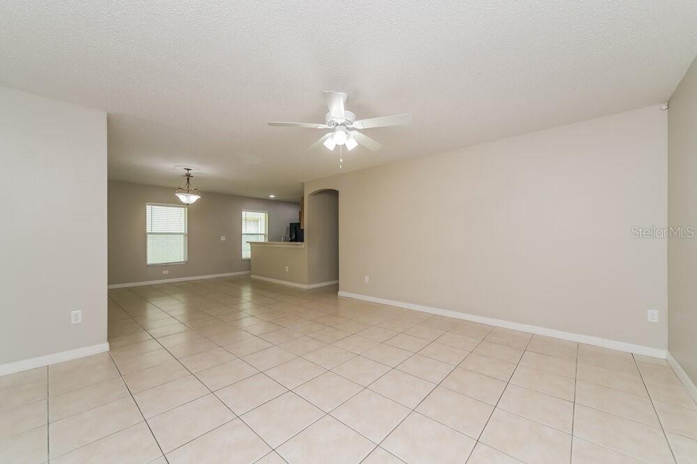 An open-concept living area features light-colored tile flooring, beige walls, and a ceiling fan — 213 OWENSHIRE CIRCLE, KISSIMMEE, FL