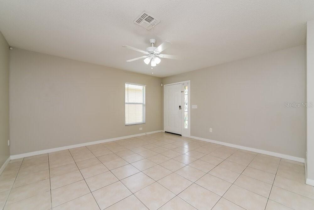 An empty room with beige walls, tile flooring, a ceiling fan, and a front door — 213 OWENSHIRE CIRCLE, KISSIMMEE, FL