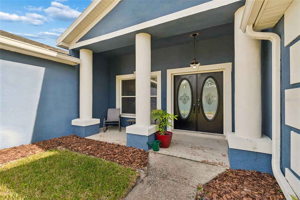 A blue house exterior features a covered porch with white columns and double front doors — 12916 ITHACA AVENUE, HUDSON, FL