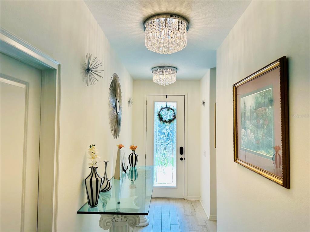 A bright entryway features two crystal flush-mount lights, a glass console table, and wall art — 944 OLD WINDSOR WAY, SPRING HILL, FL