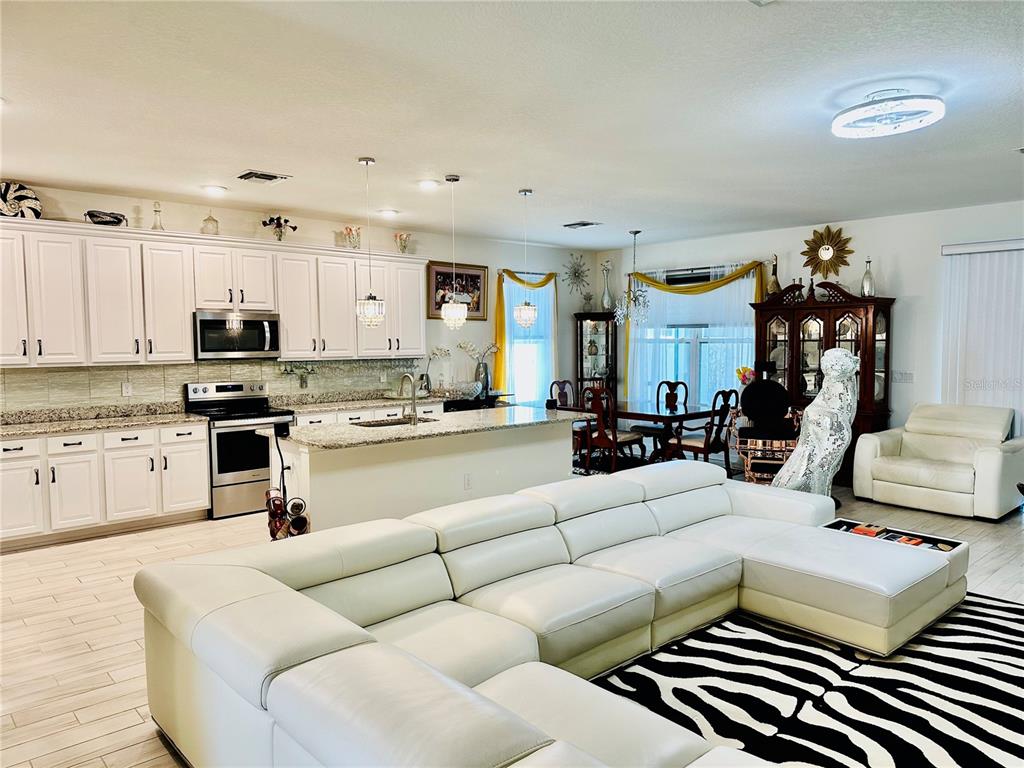 An open-concept kitchen and living area featuring white cabinetry, granite countertops, and a sectional sofa — 944 OLD WINDSOR WAY, SPRING HILL, FL