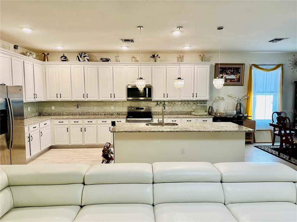 A kitchen with white cabinets, granite countertops, and a central island faces a white sofa — 944 OLD WINDSOR WAY, SPRING HILL, FL