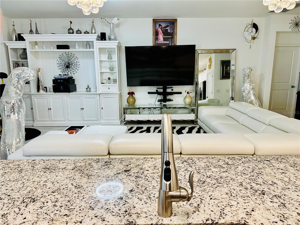 A kitchen island faucet overlooks a living room with white furniture and a large television — 944 OLD WINDSOR WAY, SPRING HILL, FL