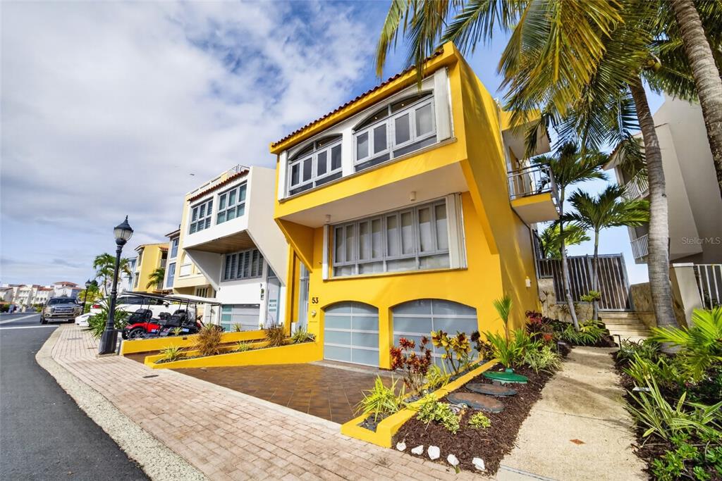 A bright yellow three-story townhouse with a two-car garage and a paved driveway — 53 ISLA SAN MIGUEL, HUMACAO, PR