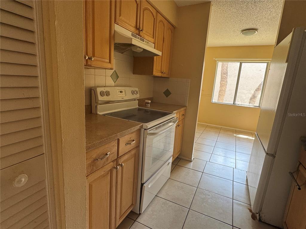 A kitchen with light wood cabinets, white appliances, and tiled floors leads to a dining area — 7512 NEEDLE LEAF PLACE UNIT 52, TAMPA, FL
