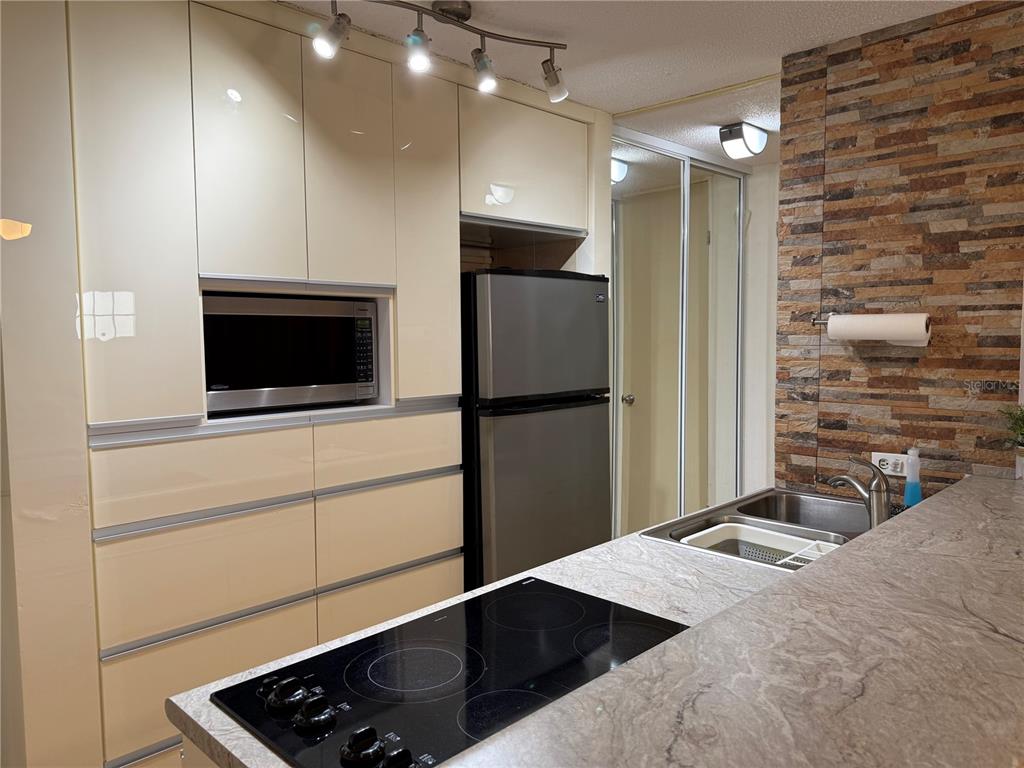 A kitchen features cream cabinets, a stainless steel refrigerator, a cooktop, and a stone backsplash — COND. LAS CABANAS CARR 466 KM 8.9 UNIT D2, ISABELA, PR