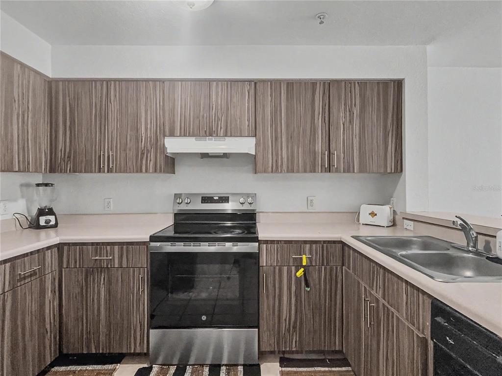 A kitchen features wood-grain cabinets, a stainless steel stove, and light-colored laminate countertops — 14049 FAIRWAY ISLAND DRIVE UNIT 122, ORLANDO, FL