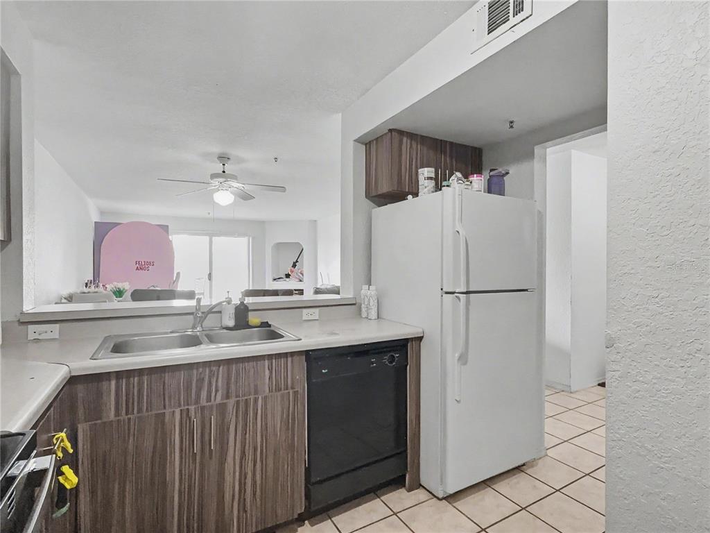 A kitchen features wood-grain cabinets, a black dishwasher, a white refrigerator, and a pass-through window — 14049 FAIRWAY ISLAND DRIVE UNIT 122, ORLANDO, FL