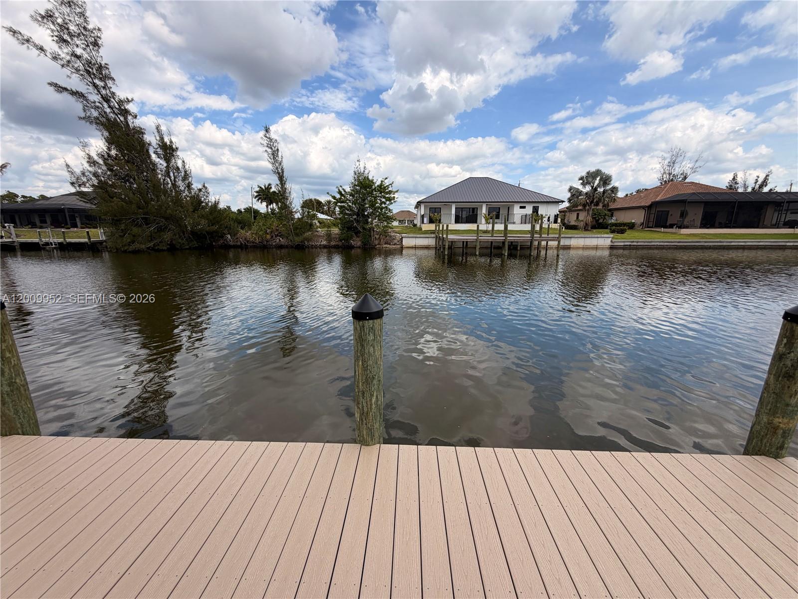 A wooden dock overlooks a canal with houses on the opposite bank under a cloudy sky — 2329 NW 36TH PL, Cape Coral FL 33993, CAPE CORAL, FL
