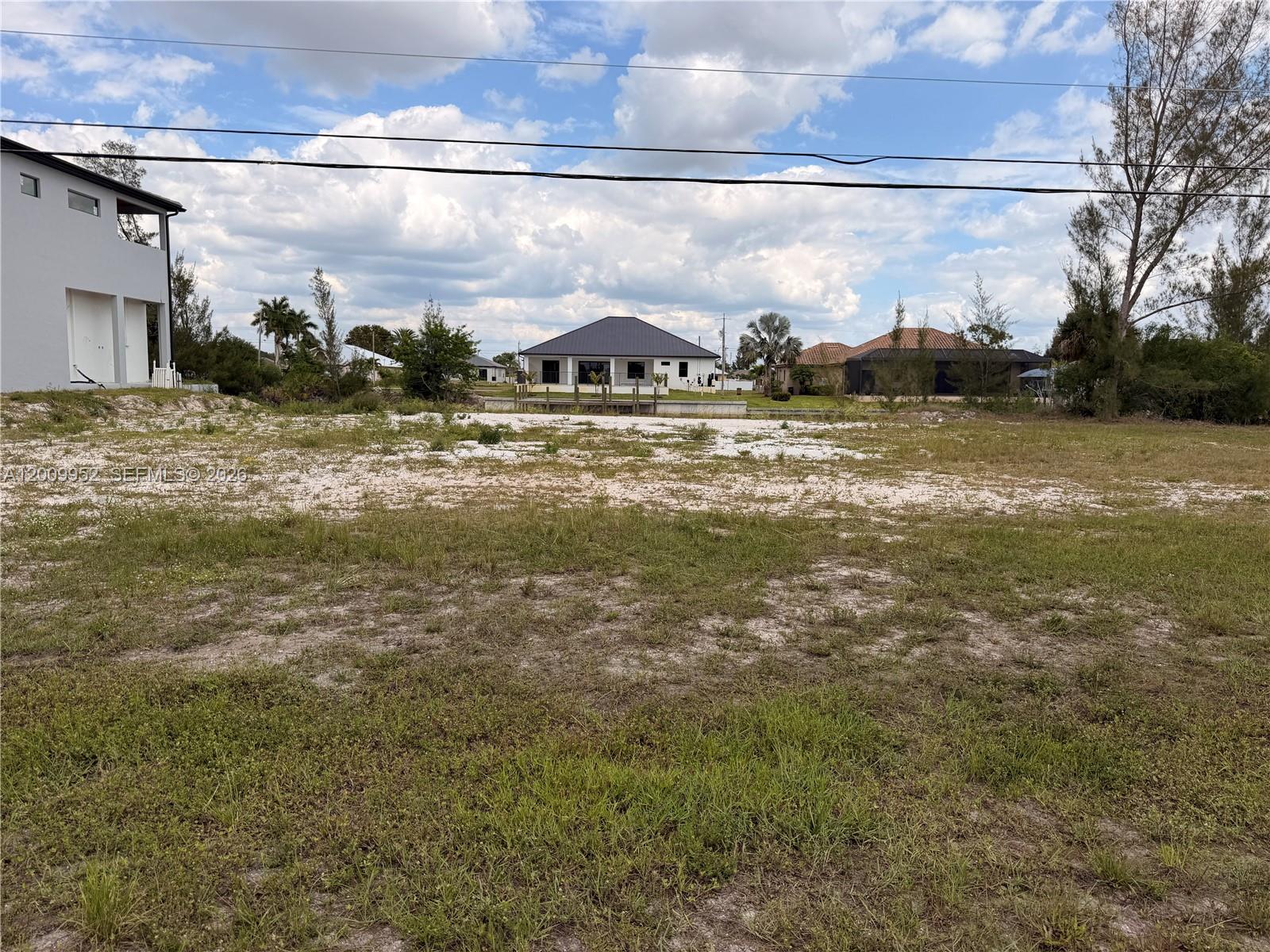 A vacant, grassy lot sits in front of a canal and several residential houses — 2329 NW 36TH PL, Cape Coral FL 33993, CAPE CORAL, FL