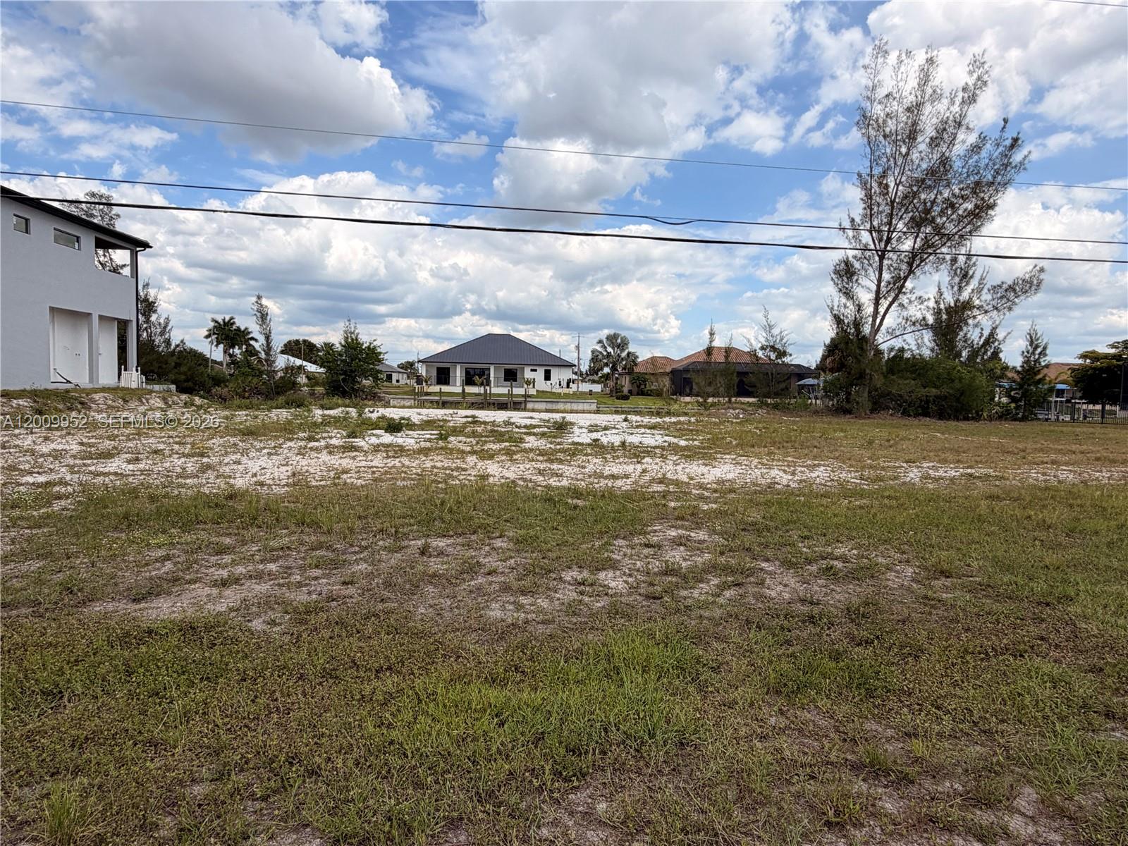 A vacant, grassy lot sits in front of a residential neighborhood under a cloudy sky — 2329 NW 36TH PL, Cape Coral FL 33993, CAPE CORAL, FL
