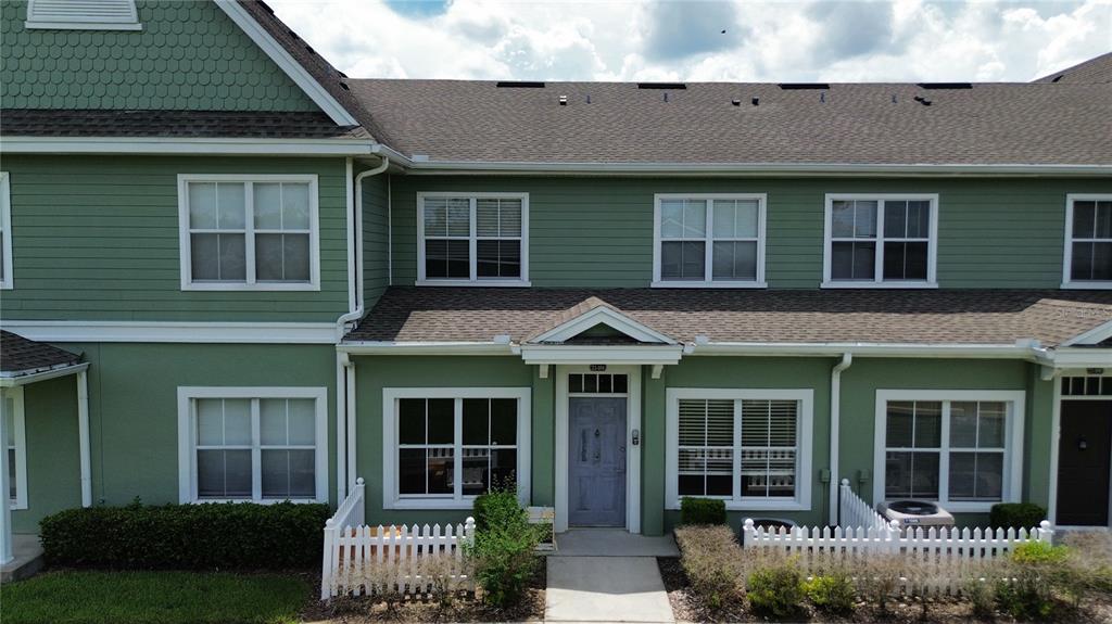 An exterior view of a two-story green townhouse with a white picket fence — 2201 SAN VITTORINO CIRCLE UNIT 104, KISSIMMEE, FL