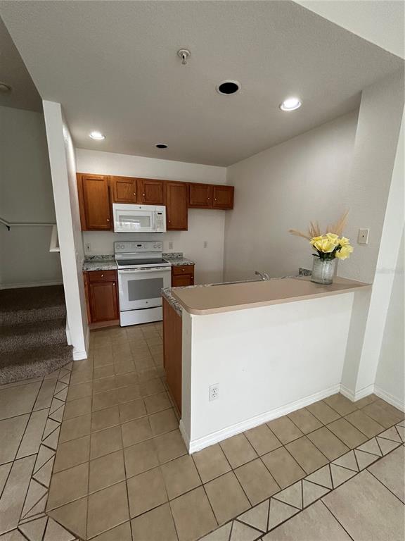 A kitchen features wood cabinets, white appliances, a breakfast bar, and tiled flooring — 2201 SAN VITTORINO CIRCLE UNIT 104, KISSIMMEE, FL