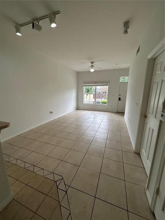 An empty living room features beige tile flooring, a ceiling fan, and track lighting — 2201 SAN VITTORINO CIRCLE UNIT 104, KISSIMMEE, FL