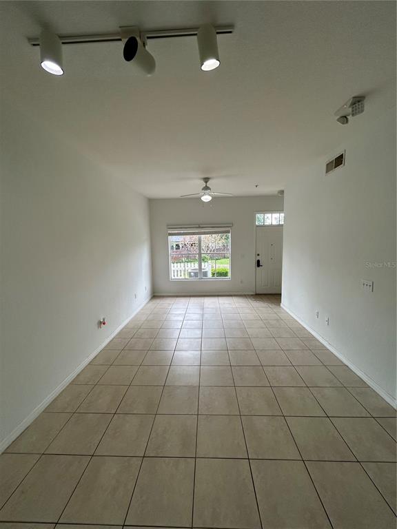 An empty room features light-colored tile flooring, white walls, a ceiling fan, and track lighting — 2201 SAN VITTORINO CIRCLE UNIT 104, KISSIMMEE, FL