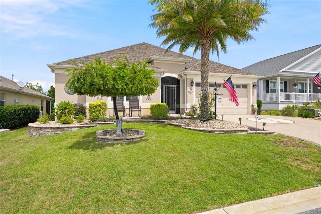 A single-story house with a palm tree, manicured lawn, and an American flag — 3095 KRAMER COURT, THE VILLAGES, FL