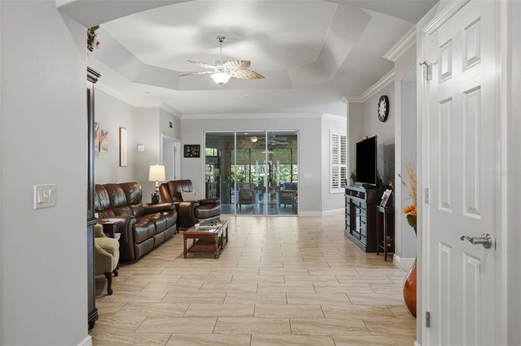 A living room with a tray ceiling, tile flooring, and sliding glass doors to a lanai — 3095 KRAMER COURT, THE VILLAGES, FL