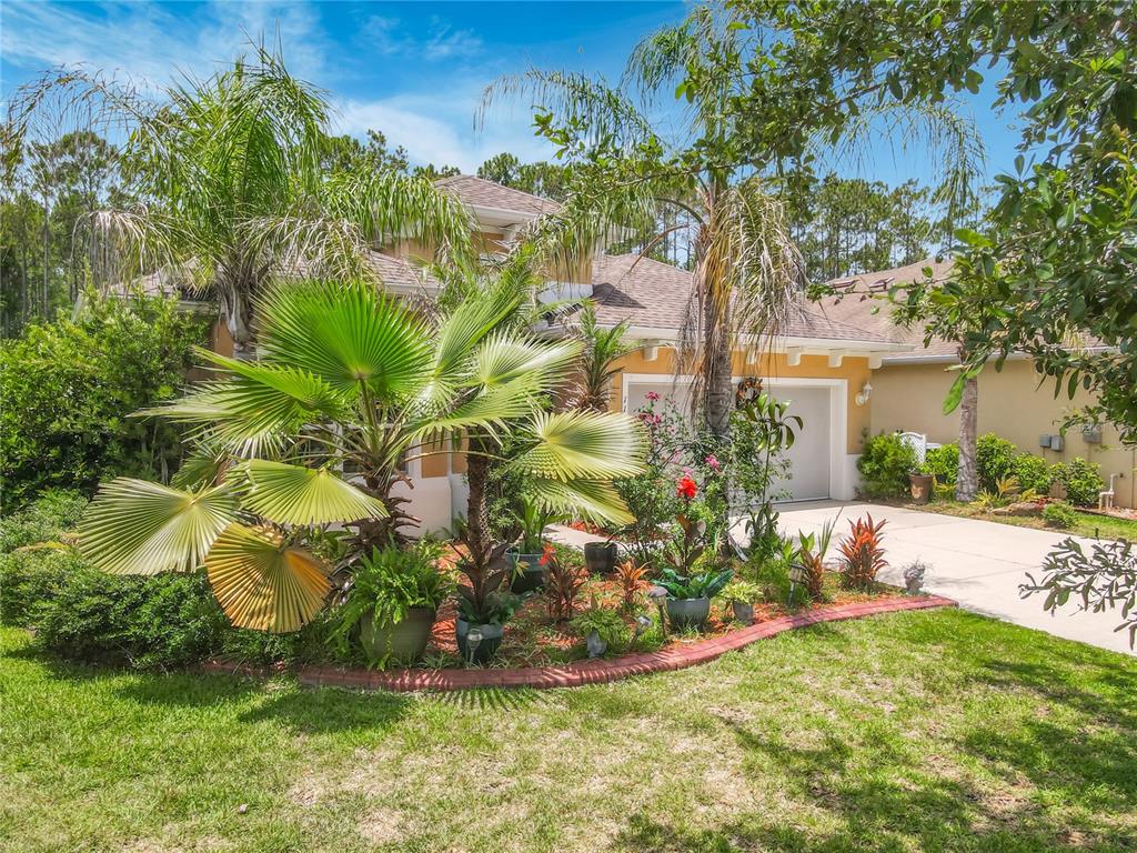 A house exterior with a landscaped front garden, palm trees, and a two-car garage — 111 S HUMMINGBIRD PLACE, PALM COAST, FL