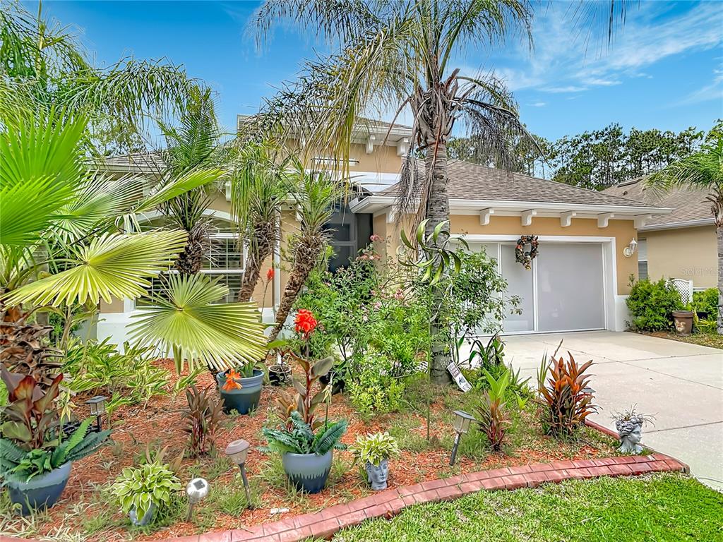 A single-story house with a tan exterior, a two-car garage, and a landscaped front yard — 111 S HUMMINGBIRD PLACE, PALM COAST, FL