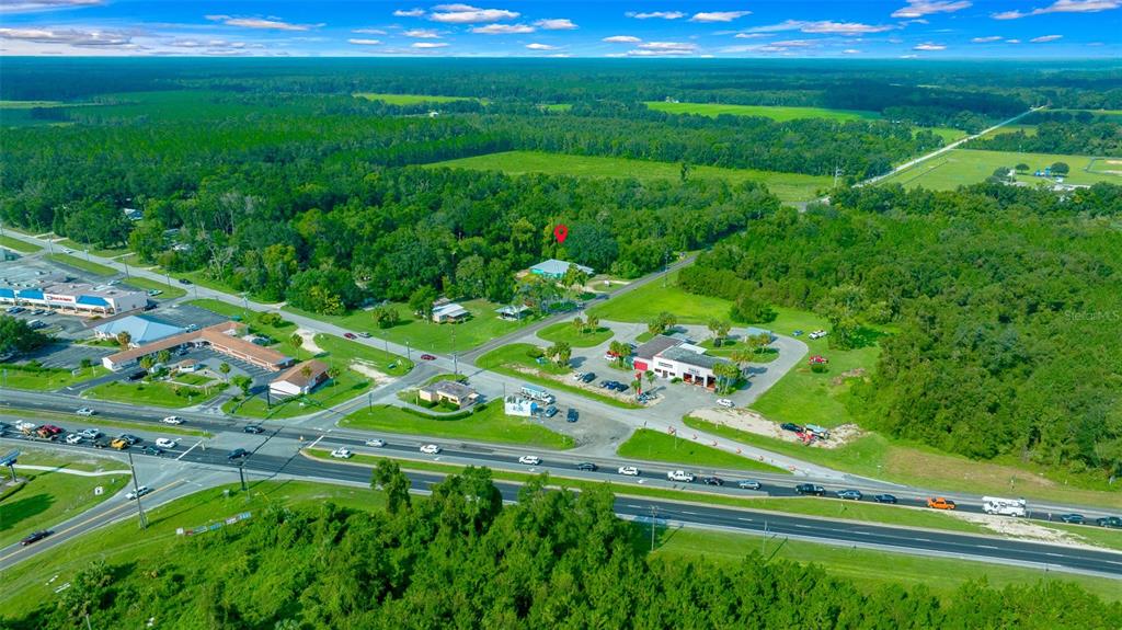 This aerial view shows a house marked with a red pin near a highway — 1415 NW 23RD AVENUE, CHIEFLAND, FL