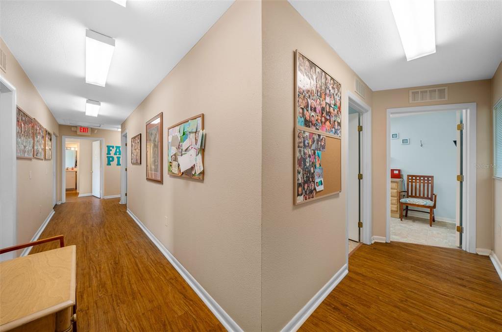 A hallway with wood-look flooring, beige walls, and a bulletin board featuring many photos — 1415 NW 23RD AVENUE, CHIEFLAND, FL