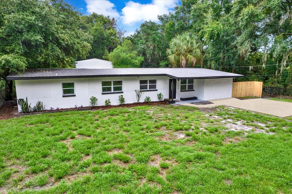 A single-story white brick house with a dark metal roof sits on a grassy lot — 3606 AUTUMN PALM DRIVE, ZEPHYRHILLS, FL