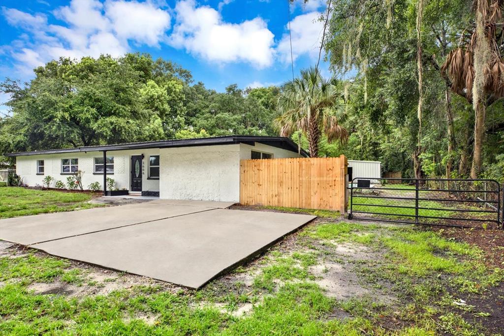 A single-story white house with a concrete driveway and a wooden fence beside a gate — 3606 AUTUMN PALM DRIVE, ZEPHYRHILLS, FL