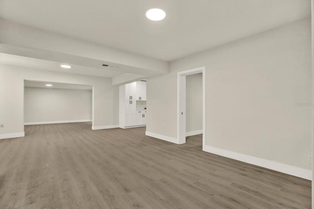 A spacious room with light gray walls, wood-look flooring, recessed lighting, and a small kitchenette — 3606 AUTUMN PALM DRIVE, ZEPHYRHILLS, FL