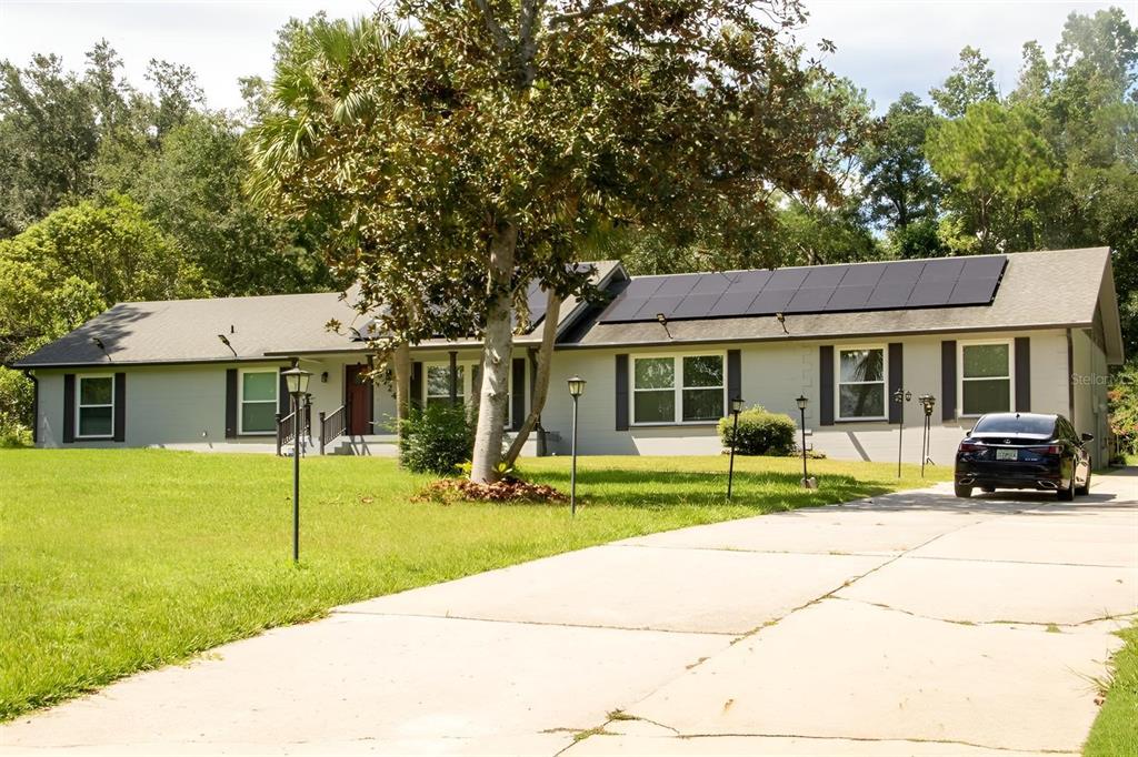 A single-story house with a gray exterior, solar panels on the roof, and a driveway — 8424 NW 2 PLACE, GAINESVILLE, FL