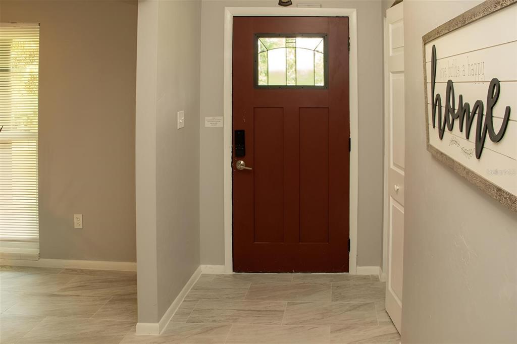 An entryway features light-colored tile flooring, gray walls, and a dark red front door — 8424 NW 2 PLACE, GAINESVILLE, FL