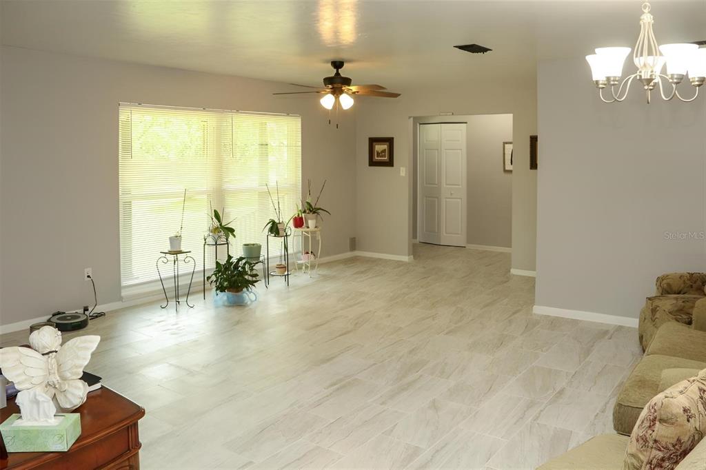 A living room features light-colored tile flooring, a ceiling fan, and a large window — 8424 NW 2 PLACE, GAINESVILLE, FL