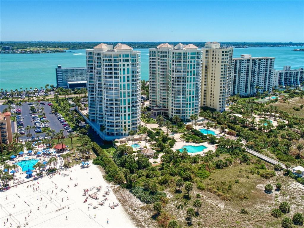 An aerial view shows high-rise residential towers near a sandy beach and swimming pools — 1170 GULF BOULEVARD UNIT 404, CLEARWATER BEACH, FL