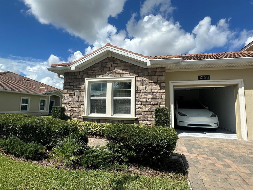 A single-story house exterior features stone veneer, a tiled roof, and a garage with a car — 1068 QUAKER RIDGE LANE, DAVENPORT, FL